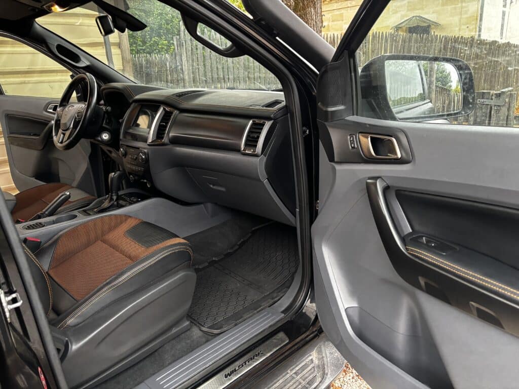 Habitacle Ford Ranger Wildtrak avec porte ouverte. Siège conducteur bicolore brun/noir, surpiqûres orange et seuil de porte WILDTRAK.