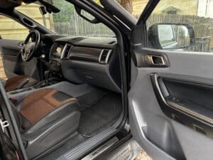 Habitacle Ford Ranger Wildtrak avec porte ouverte. Siège conducteur bicolore brun/noir, surpiqûres orange et seuil de porte WILDTRAK.