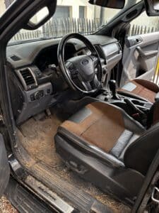 Intérieur sale du Ford Ranger Wildtrak (textes visibles) : plancher, tapis de sol en caoutchouc et sellerie cuir/tissu marron.