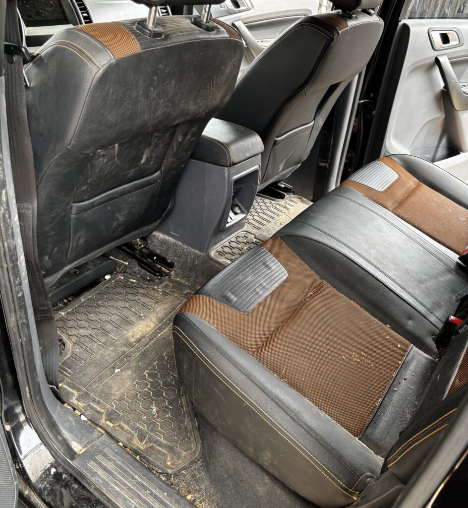 Intérieur de véhicule 4x4 extrêmement sale. Sièges noir et orange, tapis de sol en caoutchouc boueux. Détails du désordre avant nettoyage.