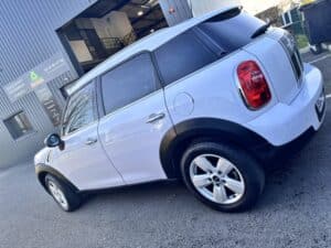 MINI Countryman blanc bandes noires, garé devant un garage proposant POÊLES, INSERTS, CHEMINÉES. Tél : 05 57 04 27 36.