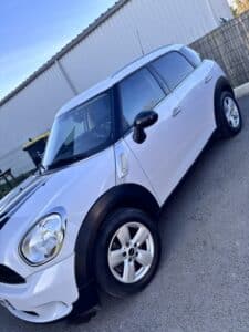 MINI Countryman blanc, vue latérale, avec bandes sport noires. Jantes alliage argentées, rétroviseurs noirs et garnitures de roues SUV.