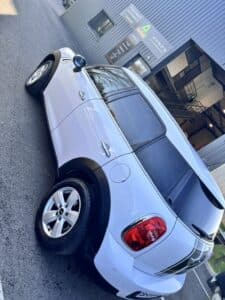 MINI Countryman blanche, jantes alu. Devant un atelier affichant "POÊLES INSERTS BOIS/GRANULÉS CHEMINÉES" et le tél : 05 57 04 27 36.