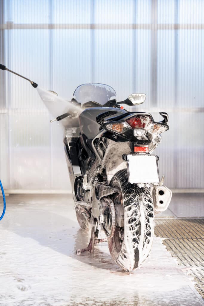 Lavage haute pression d'une moto avec mousse Motonette couverte de mousse lavée à haute pression dans une station de lavage lumineuse.