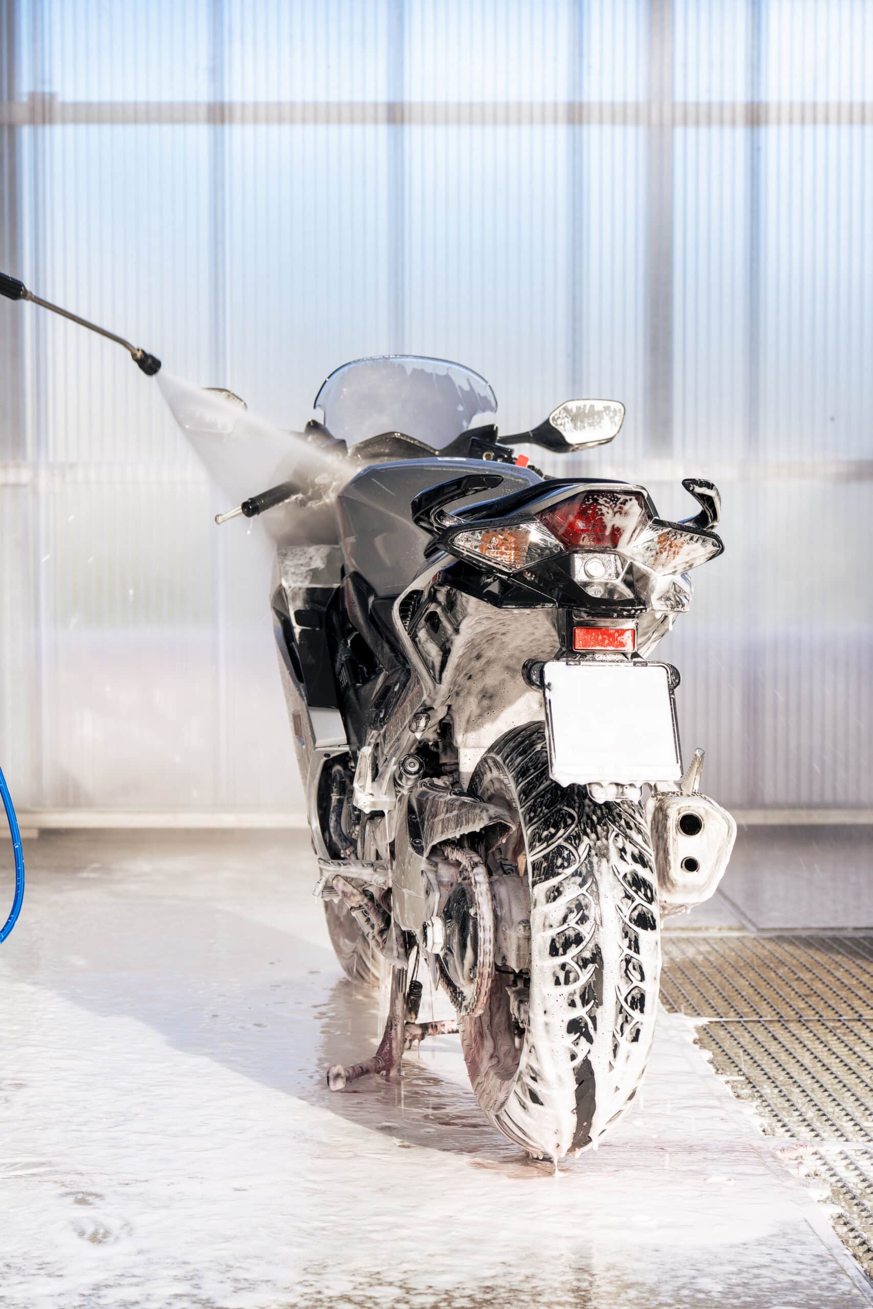 Motonette couverte de mousse lavée à haute pression dans une station de lavage lumineuse.