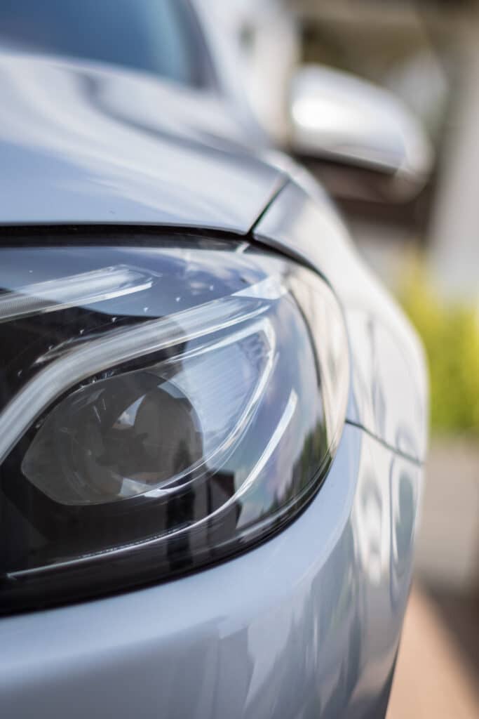 Phare Avant Voiture Moderne Gris : Détail Design Gros plan sur le phare avant d'une voiture moderne gris clair, mettant en valeur les réflecteurs et le design épuré.