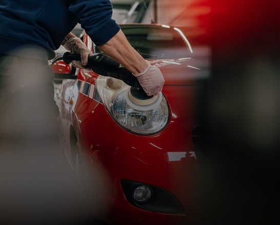 Polissage professionnel d'un phare de voiture rouge à l'aide d'une polisseuse électrique, mains gantées visibles.