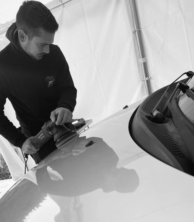 Detailing auto : Polissage expert de la carrosserie JD Détailer JD polissant le capot d'une voiture avec une polisseuse. Reflet de l'action sur la peinture pour un detailing professionnel.