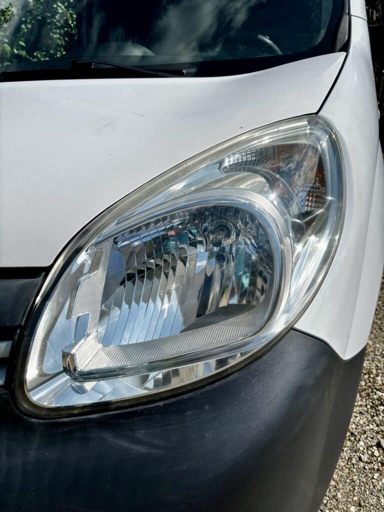 Phare d'utilitaire blanc – Gros plan sur l'optique brillante. Phare avant d'un utilitaire blanc brillant. Reflets lumineux sur l'optique claire et le pare-chocs noir texturé.