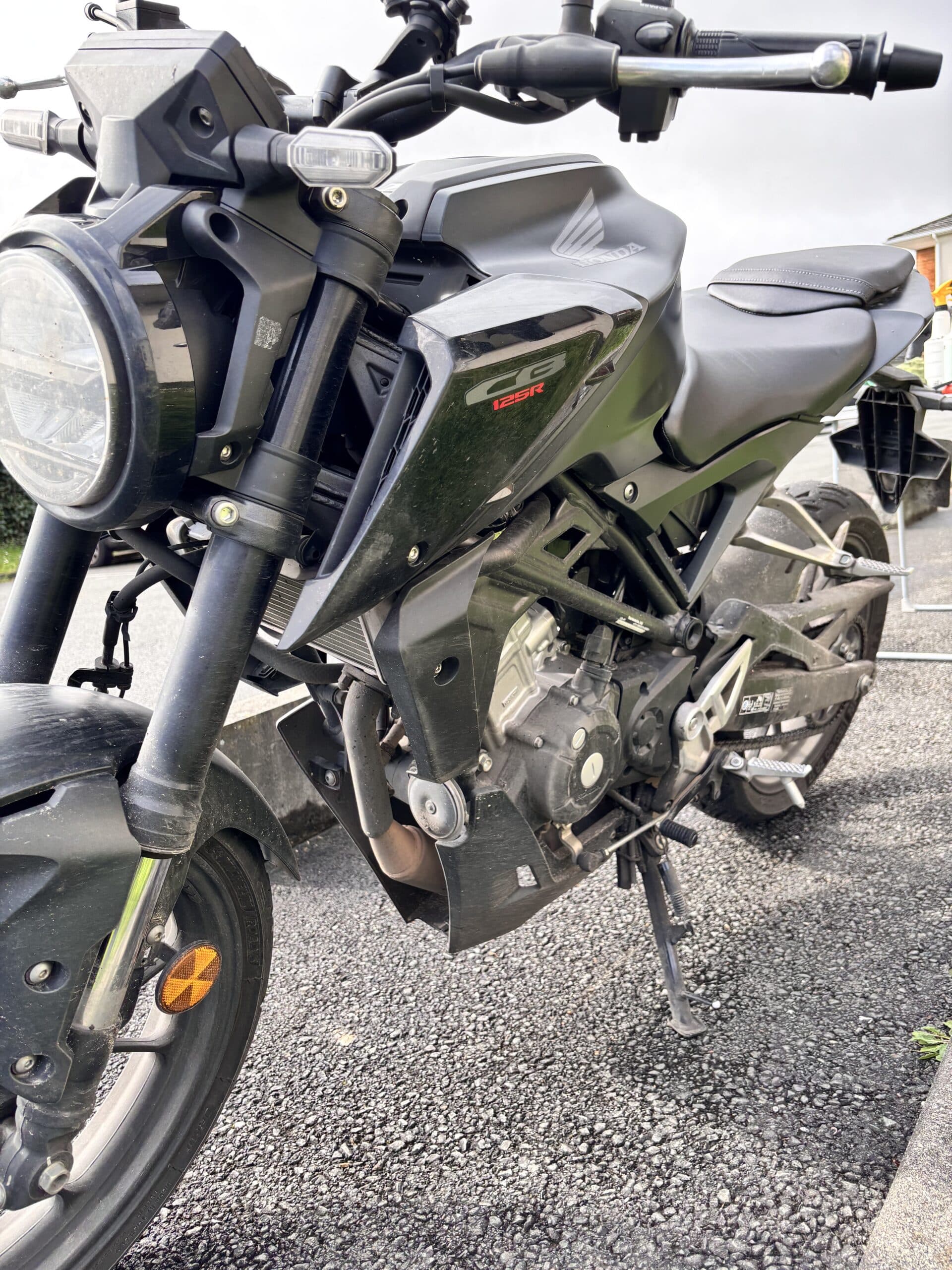 Moto Honda CB125R noire avec phare rond à LED et logo CB125R visible sur le carénage latéral.