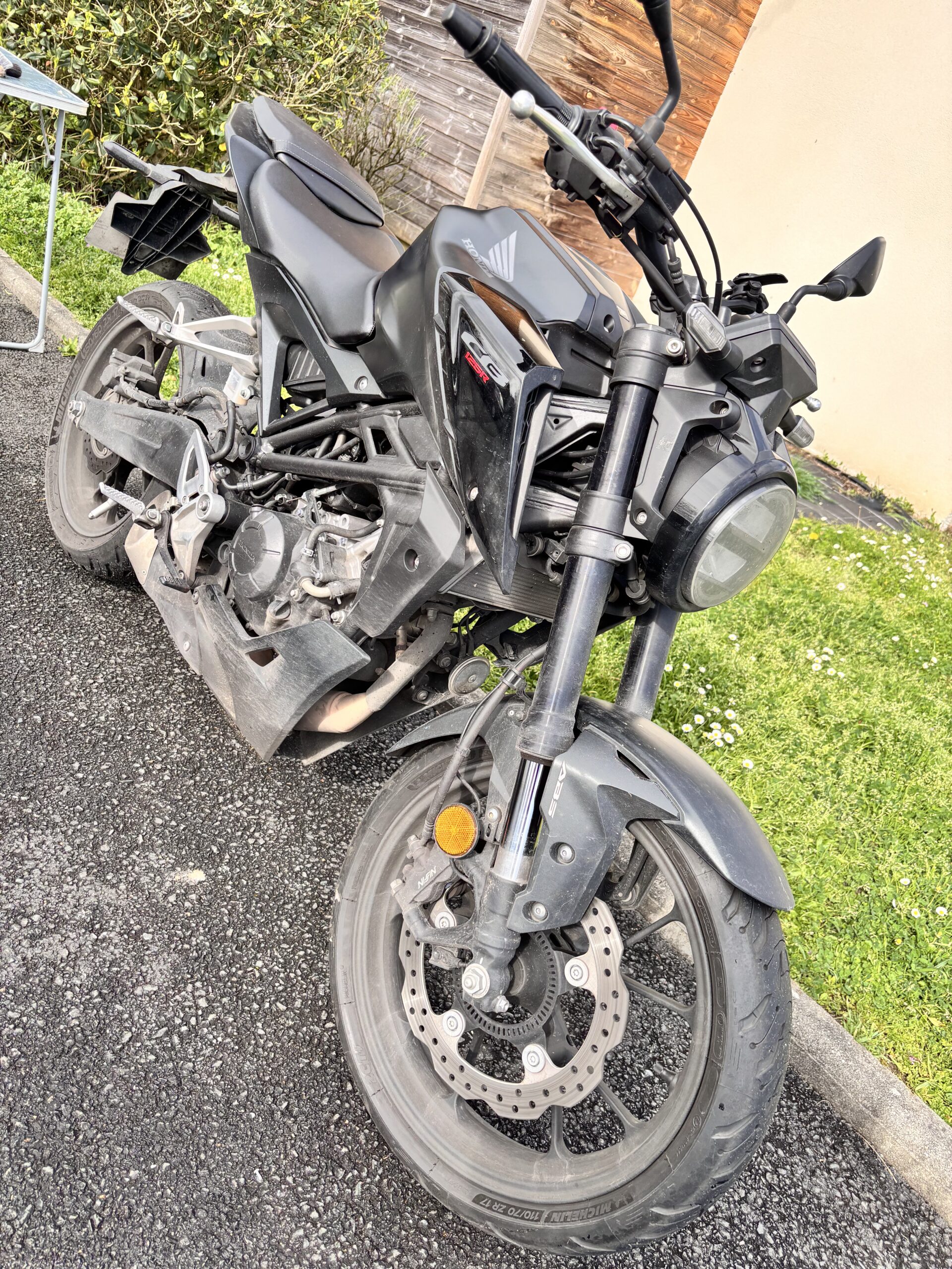 Moto Honda CB125R noire de type roadster stationnée sur l'asphalte avec logo Honda et texte CB 125R visibles.