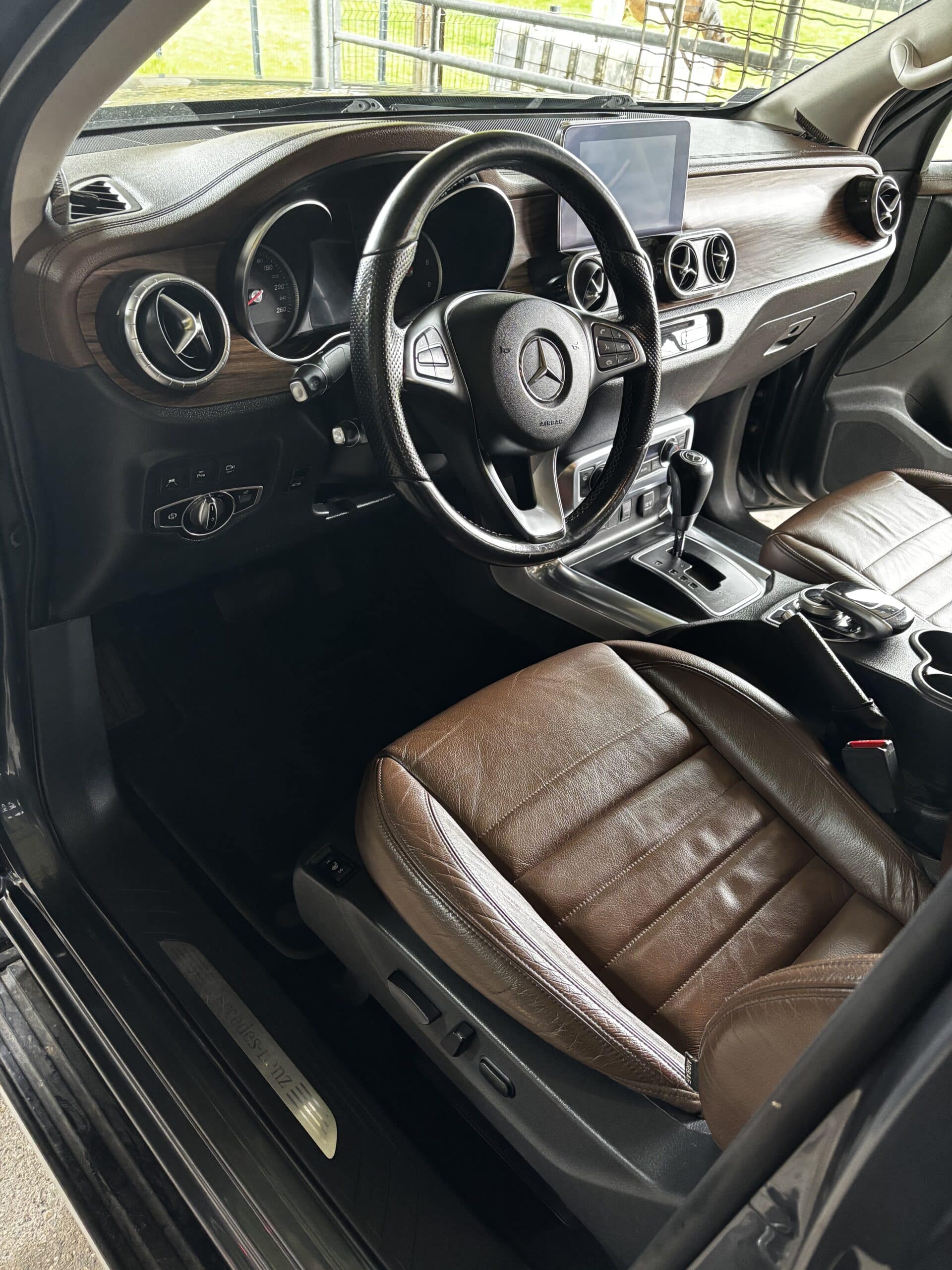 Intérieur de Mercedes-Benz Classe X avec sièges en cuir marron, tableau de bord effet bois et logo sur le volant.