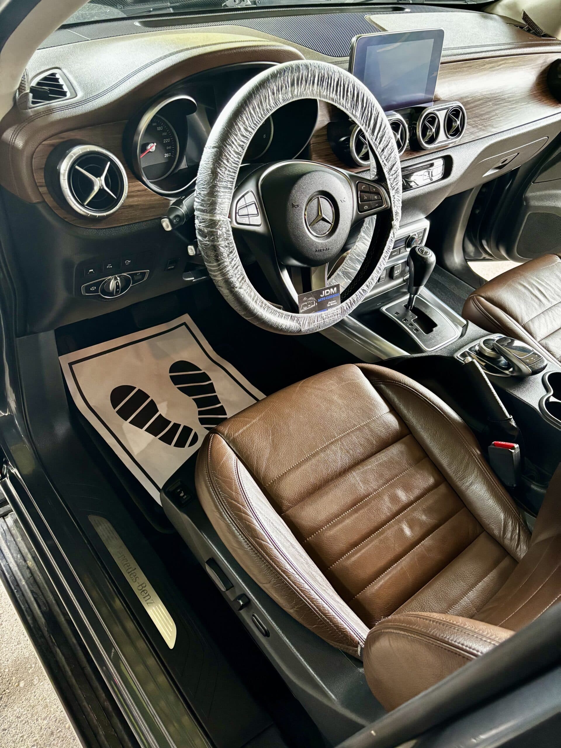Habitacle Mercedes-Benz : sièges en cuir marron, inserts bois et volant protégé par JDM Auto Cleaning.