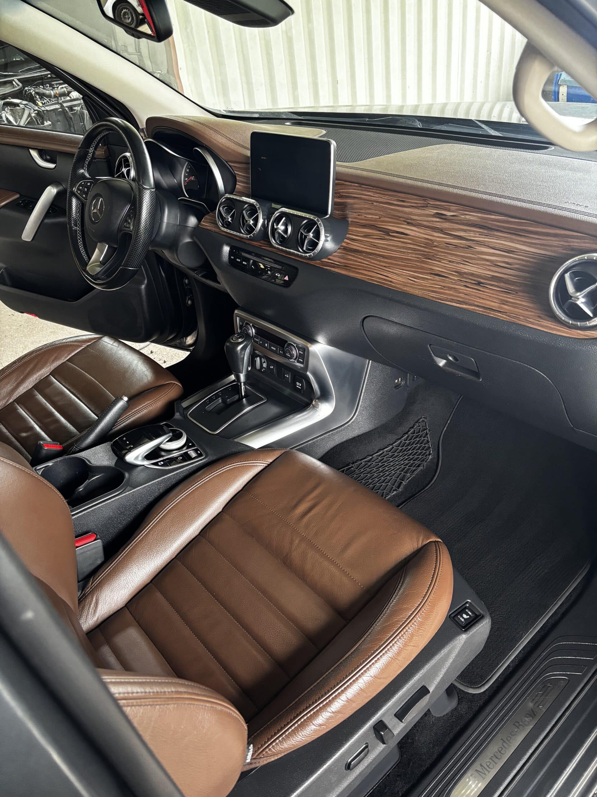 Habitacle Mercedes-Benz : sièges en cuir marron, tableau de bord en bois et logo gravé sur le seuil de porte.
