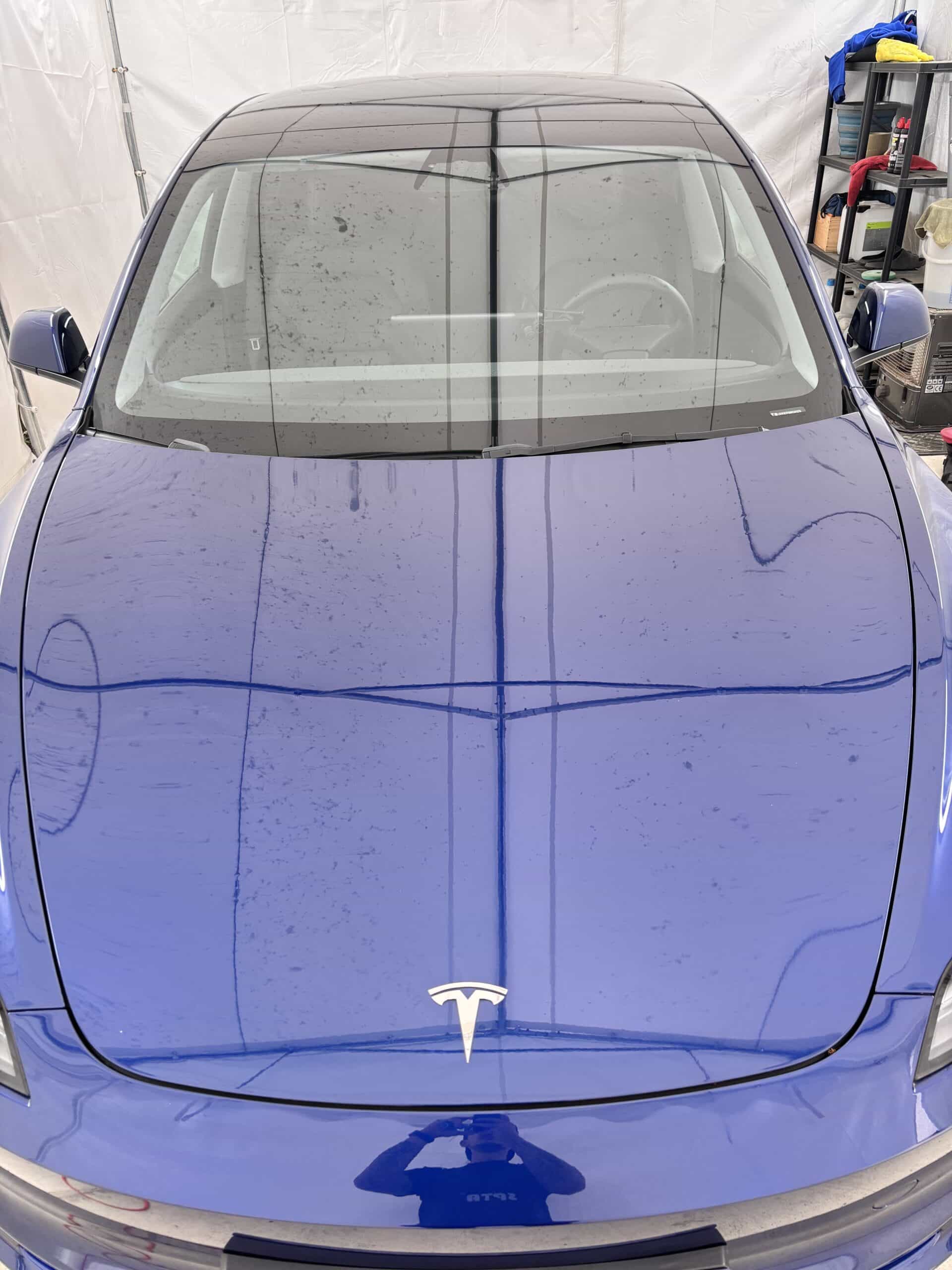 Vue de face d'une Tesla bleue brillante avec logo argenté, stationnée sous une structure blanche.