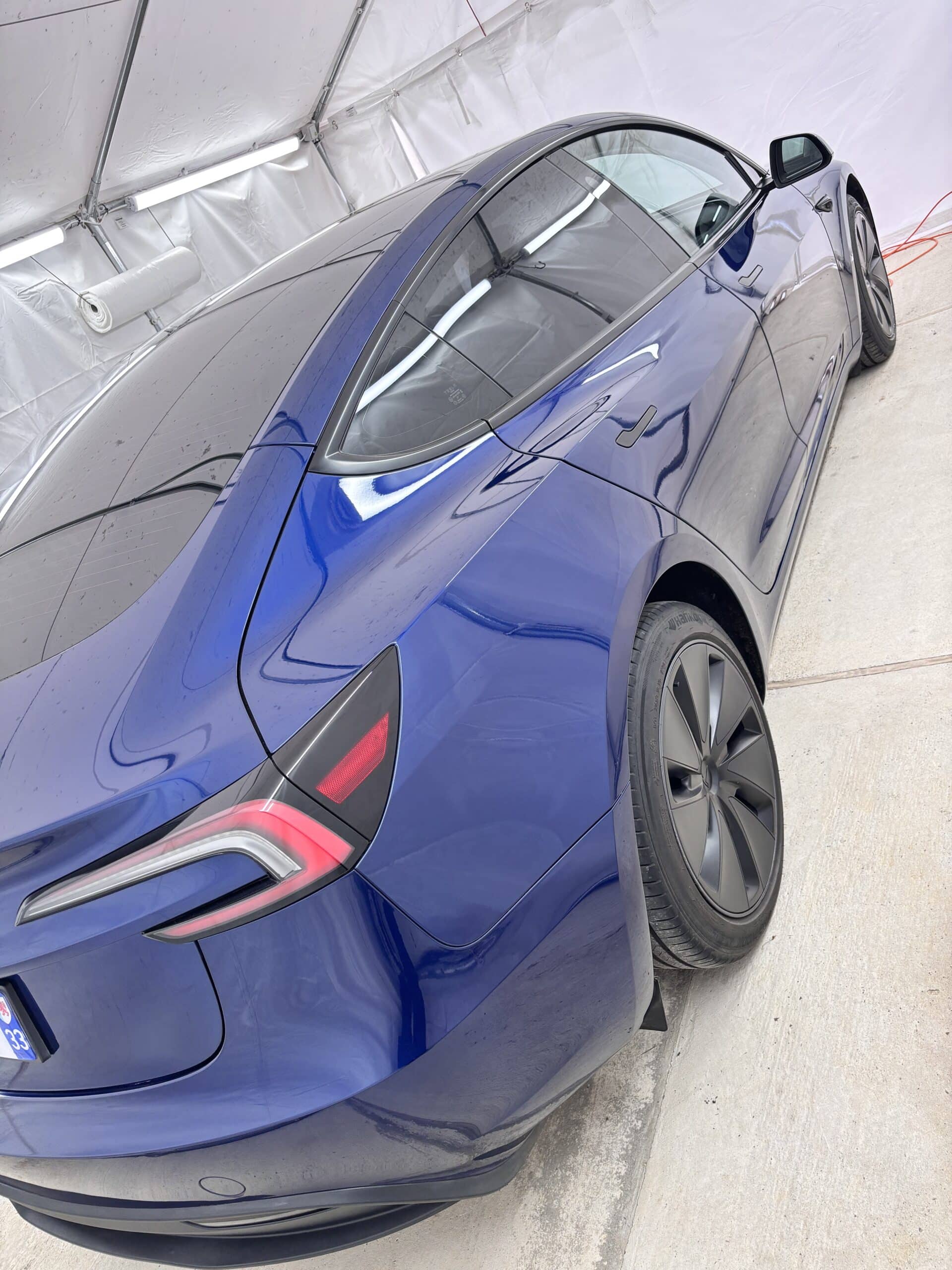 Tesla Model 3 bleu métallisé avec nouvelles jantes noires et feux arrière, dans un atelier de préparation.