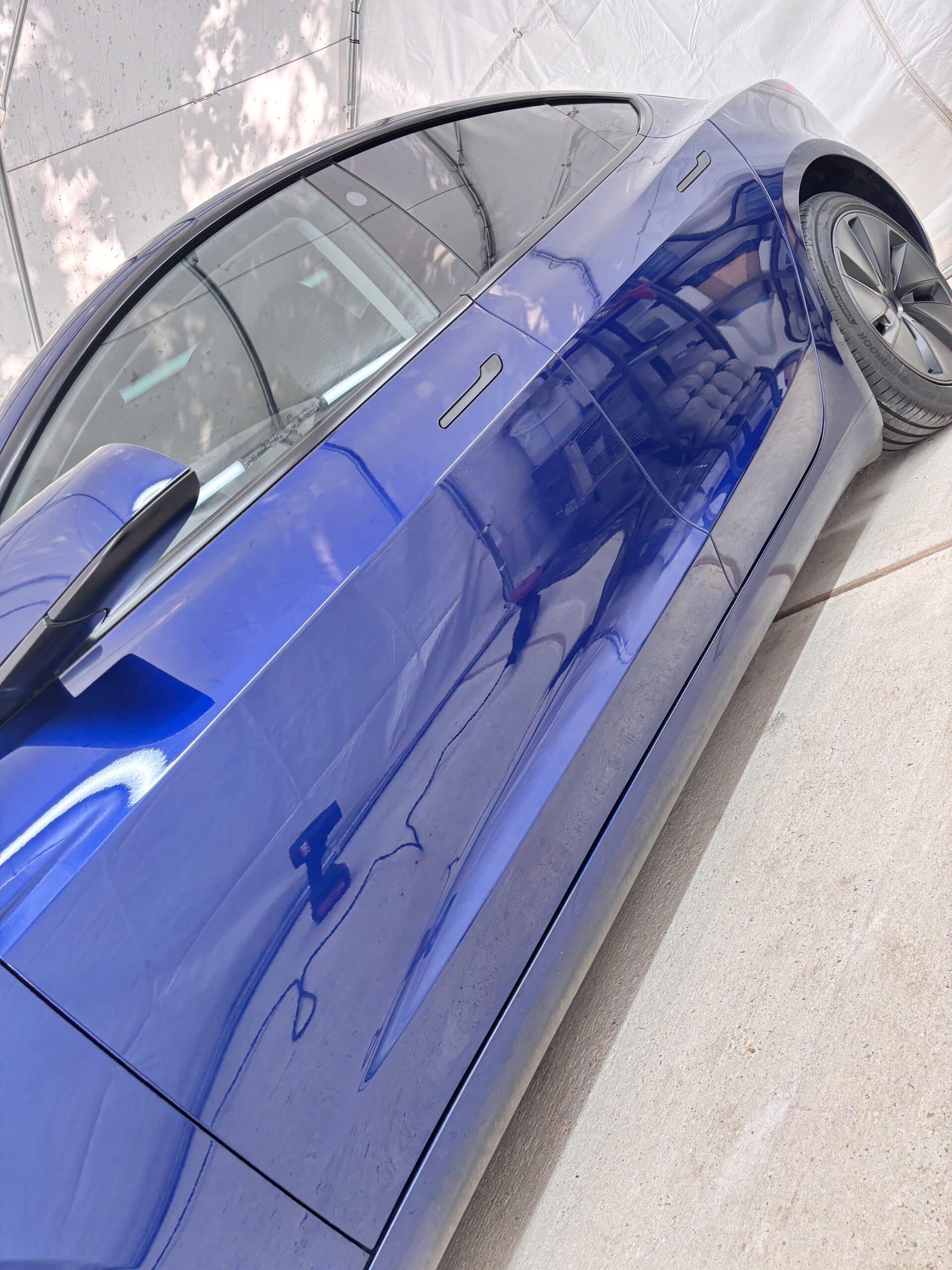 Profil d'une Tesla Model 3 bleue avec peinture effet miroir et jantes aérodynamiques Hankook.
