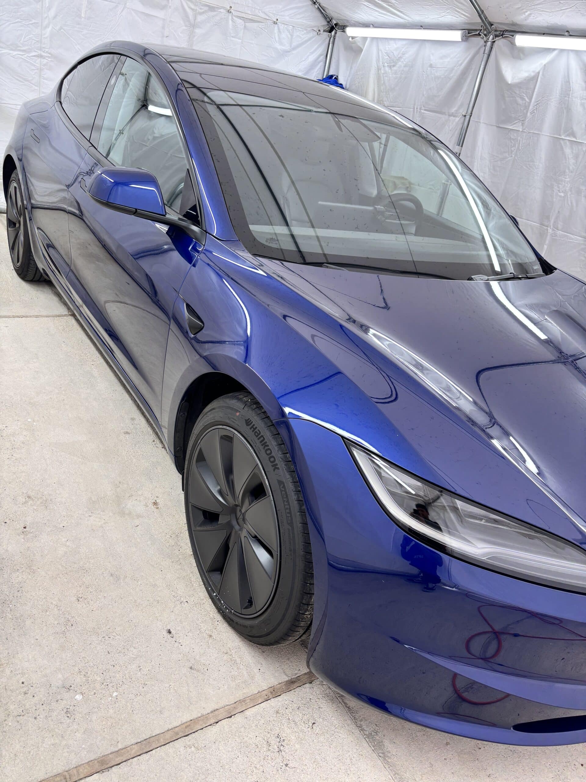 Tesla Model 3 bleue Highland avec jantes noires et pneus Hankook sous un abri de detailing.