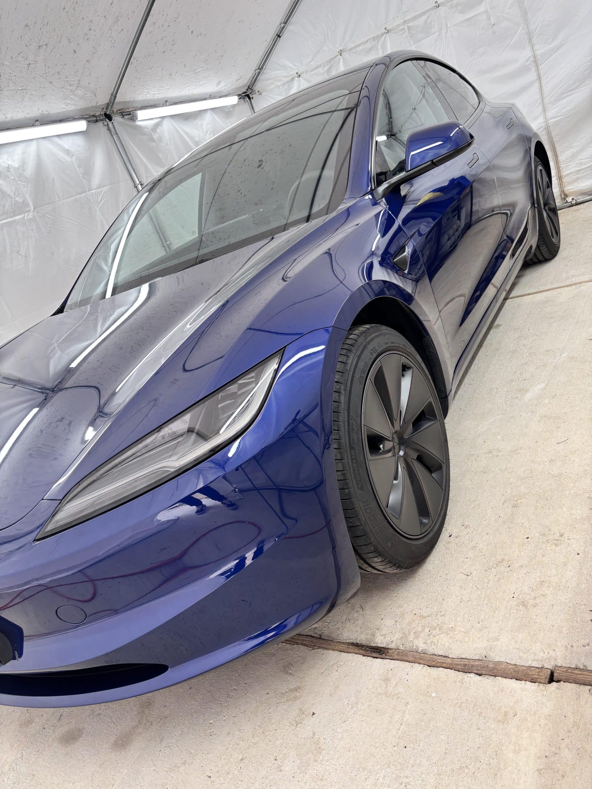 Tesla Model 3 Highland bleue brillante avec jantes noires sous les projecteurs d'un atelier de detailing.